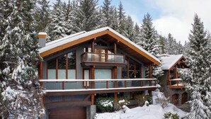 Une grande cabane en bois dotée d’un balcon, entourée d’arbres couverts de neige.