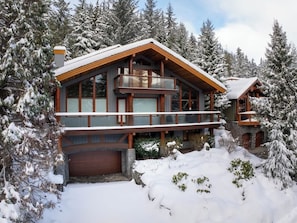 A large wooden cabin with a balcony, surrounded by snow-covered trees.