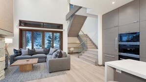 A modern living room with a grey sofa, a coffee table, and a staircase leading to an upper level. - Lakeside townhouse w/ private garage (Whistler)