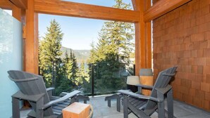 A wooden balcony with two Adirondack chairs and a small table, overlooking a forested mountain area. - Lakeside townhouse w/ private garage (Whistler)