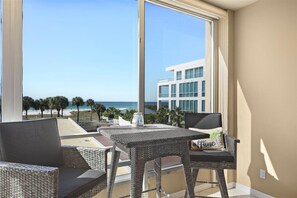 Ein Balkon mit Korbmöbeln, einem Tisch und Blick auf das Meer und die Gebäude.