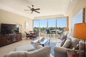 A spacious living room with a television, comfortable seating, a dining area, and large windows offering a view.