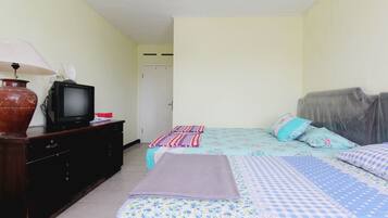 A bedroom with a bed, a television on a dresser, and a door in the background.