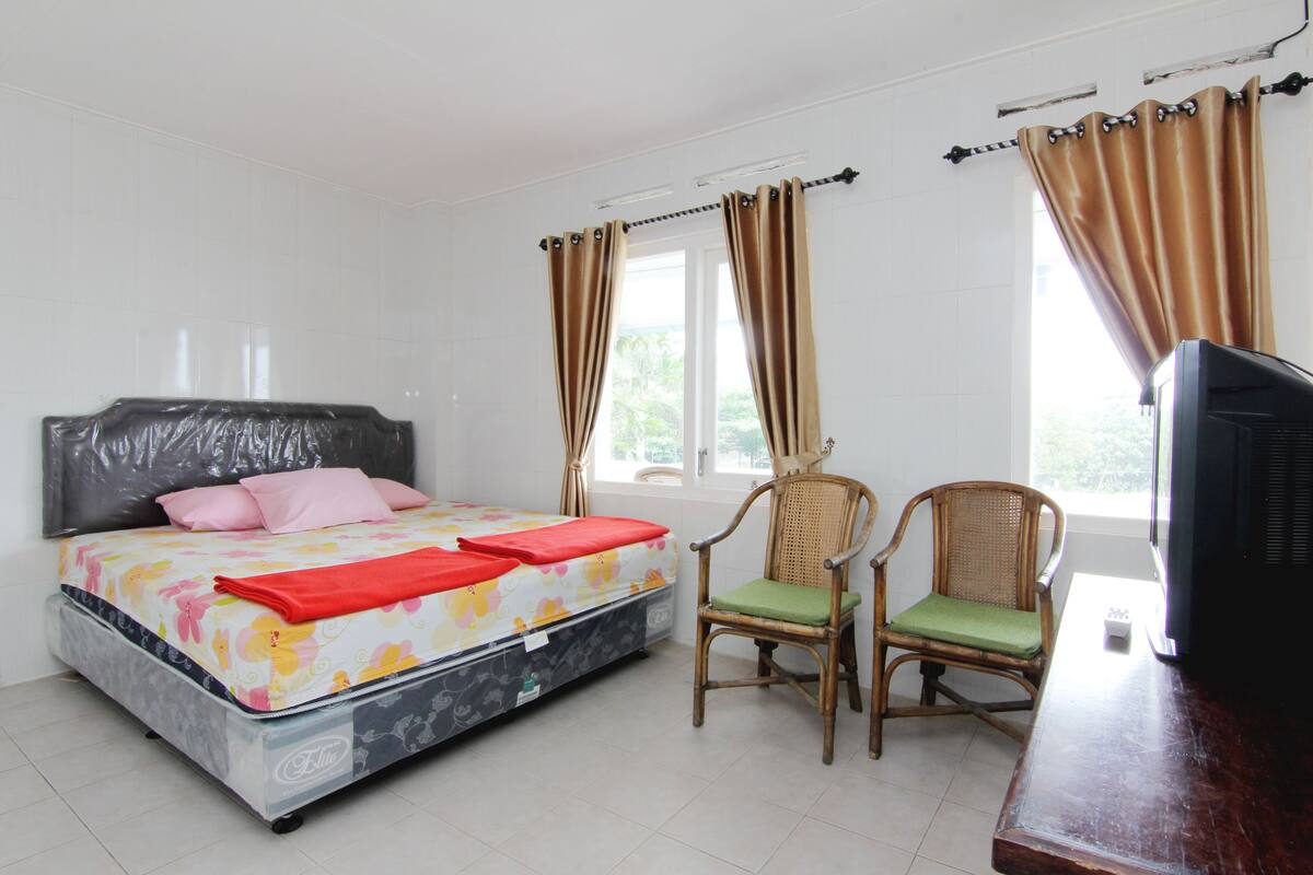 A bedroom with a bed, two chairs, a television, and curtains.