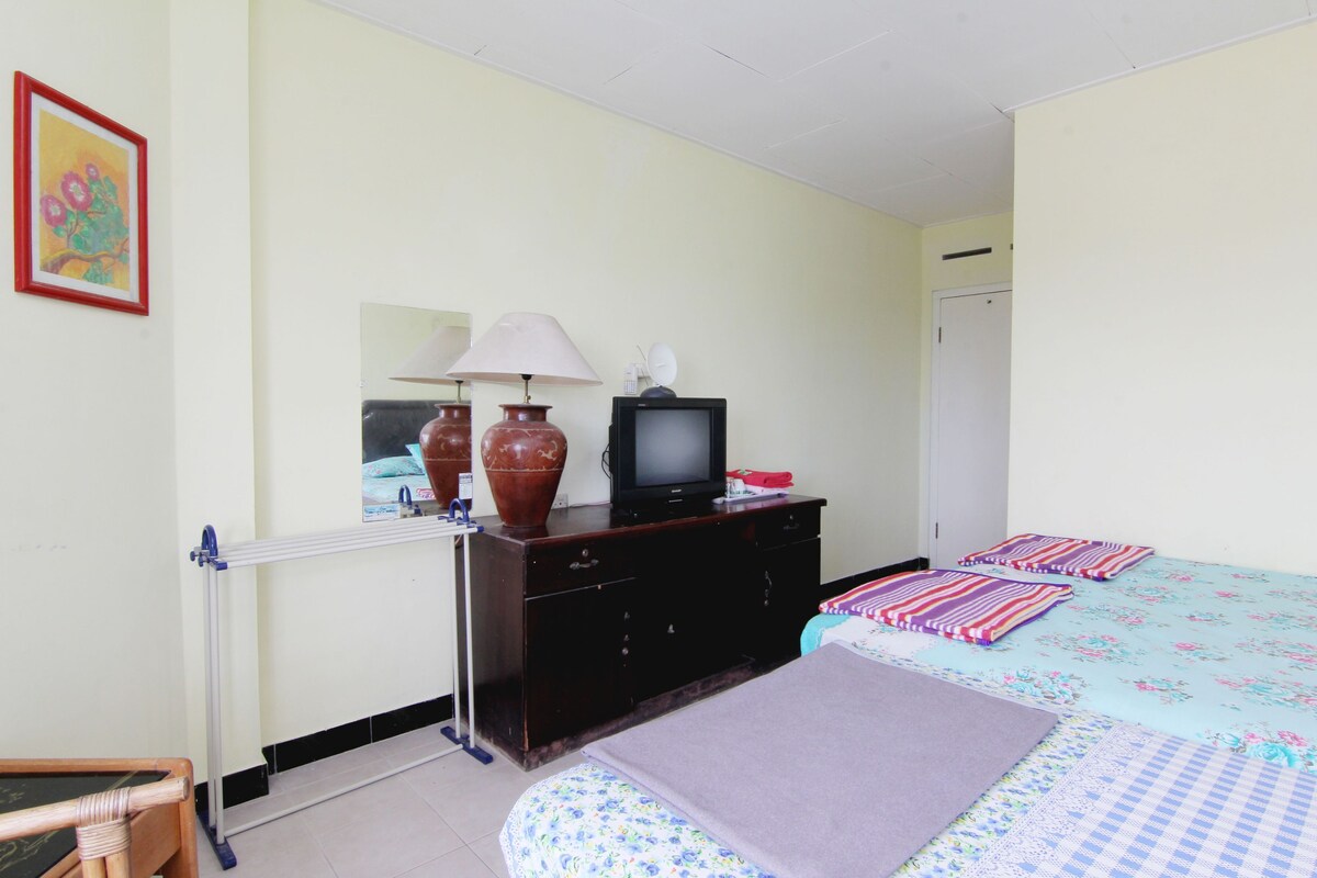 A hotel room with a bed, a TV on a dresser, a lamp, and a radiator.