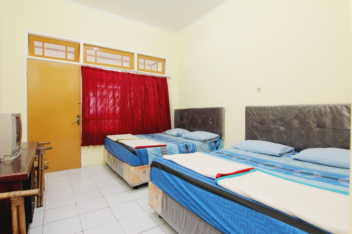 A room with two beds, a wooden desk, and a red curtain.