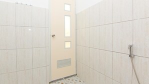 Un pequeño cuarto de baño con azulejos, una puerta, un cabezal de ducha y una rejilla de ventilación.