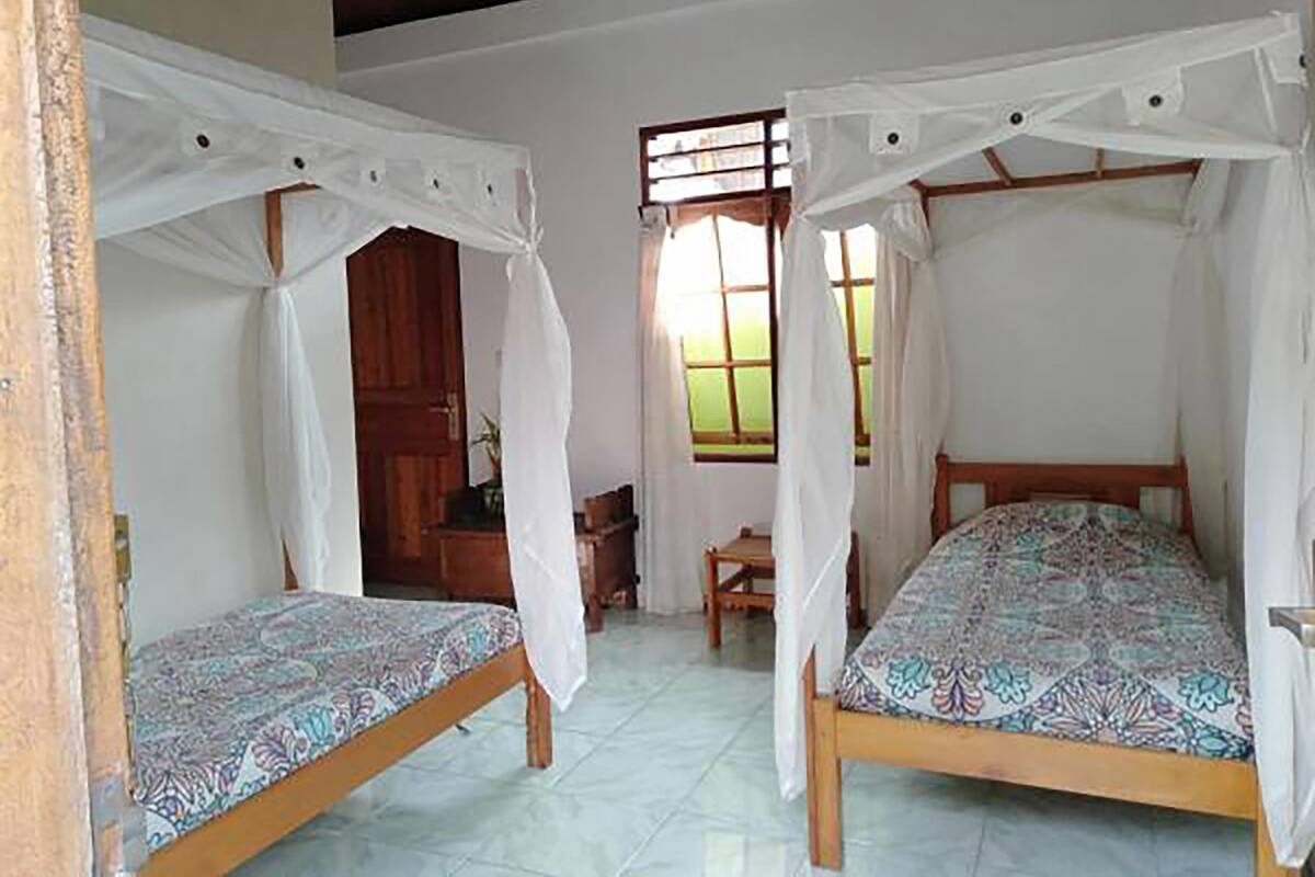 A room with two wooden beds, each with a canopy. There is a wooden door and a window with curtains.
