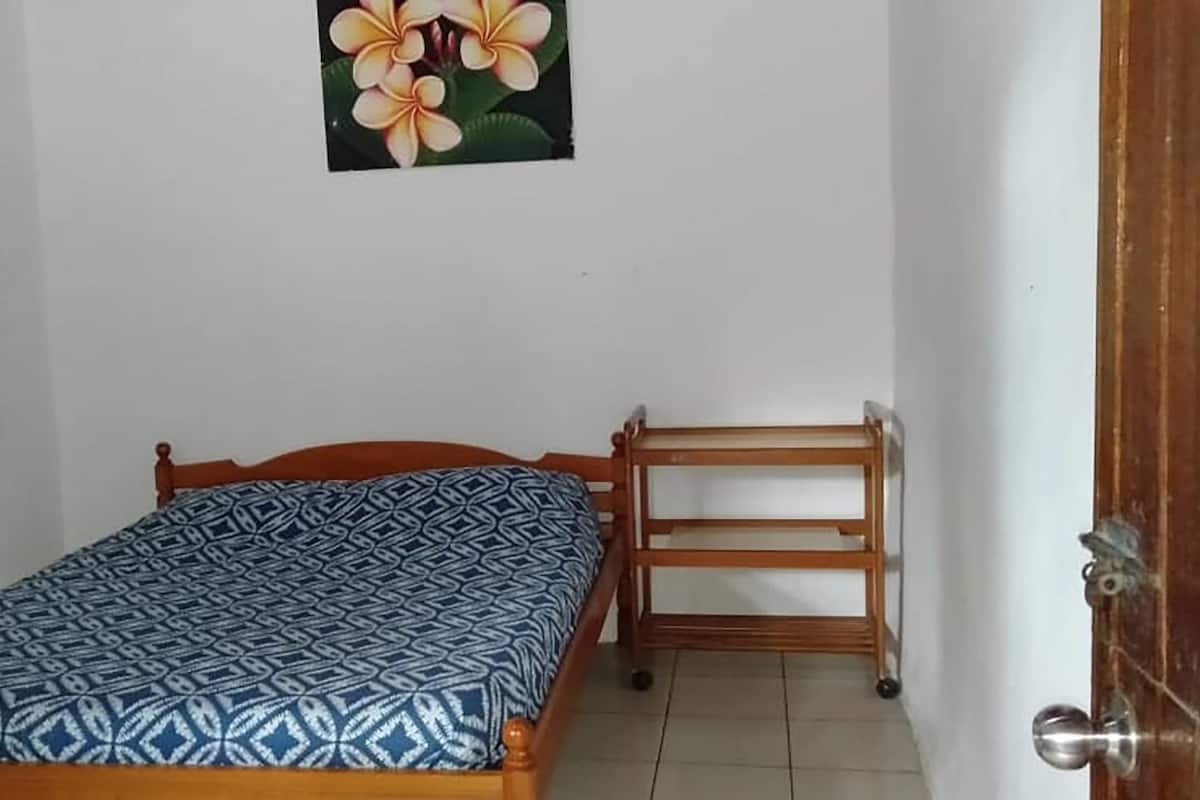 A single bed with a patterned bedspread, a wooden nightstand, and a wall-mounted picture of flowers.