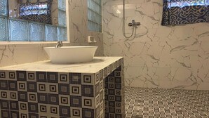 A bathroom with a white sink, a mirror, a shower, and patterned tiles. - Bagus Bay Guest House (Samosir)