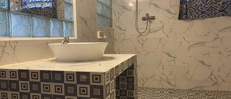 A bathroom with a white sink, a mirror, a shower, and patterned tiles.