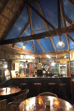A rustic interior with a high ceiling, wooden beams, and a bar area with stools and a counter. - Bagus Bay Guest House (Samosir)