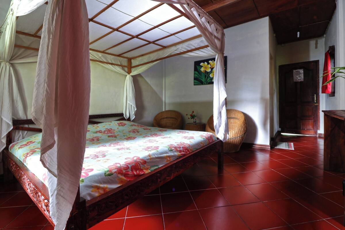 A room with a bed under a canopy, a wooden door, and a wall with a painting.