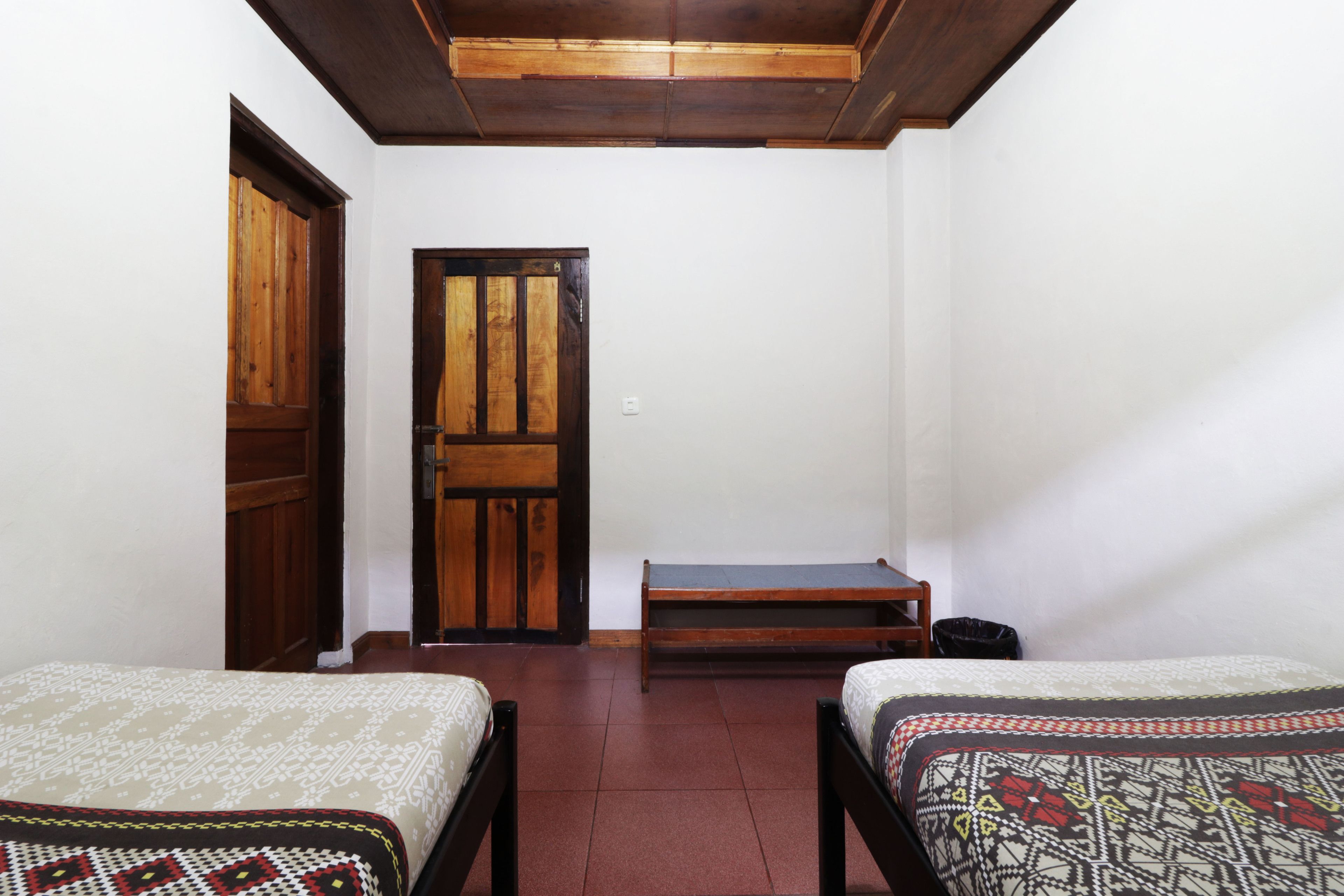 A room with two beds, a wooden door, and a bench.