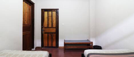 A room with two beds, a wooden door, and a bench.