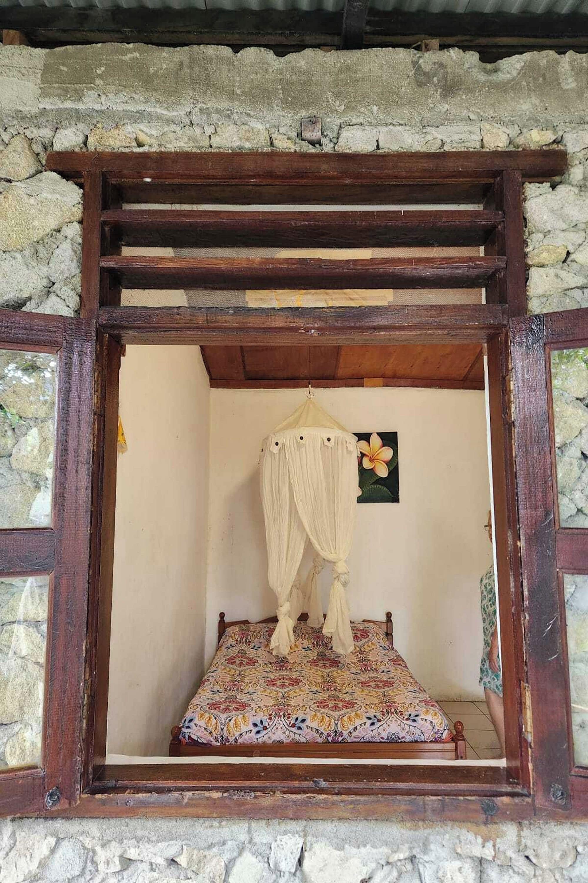 Una habitación con una cama, un ventanal de madera y una pared de piedra.