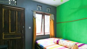 A room with a bed, a window with curtains, a door, and a green wall. - Penginapan Villa Surya Alam (Prigen)