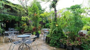 An outdoor patio area with tables and chairs, surrounded by lush greenery and potted plants. - Labuana Homestay and Cafe Garden Makassar (Makassar)