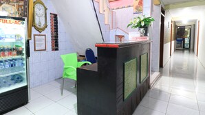 A reception area with a counter, a clock, a refrigerator with drinks, and a green chair. - Dharmawati Homestay (Sidoarjo)