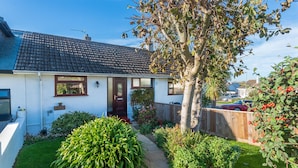Ein eingeschossiges Haus mit Ziegeldach, einer Haustür und einem kleinen Garten mit verschiedenen Pflanzen und einem Baum.
