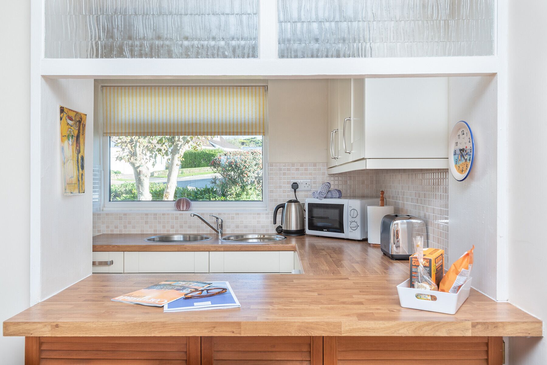 A compact kitchen with white cabinets, a wooden countertop, a kettle, a toaster, and a microwave.