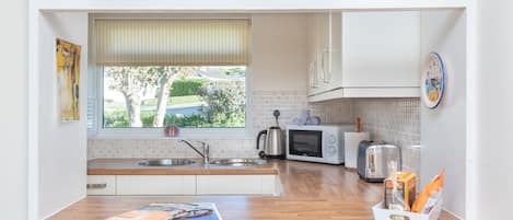 A compact kitchen with white cabinets, a wooden countertop, a kettle, a toaster, and a microwave.