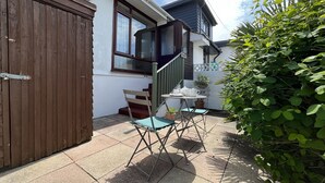 Ein Wohnhaus mit einem Holztor, einer Treppe, die zu einem Balkon führt, einer kleinen Terrasse mit Tisch und Stühlen und einem Blumentopf.