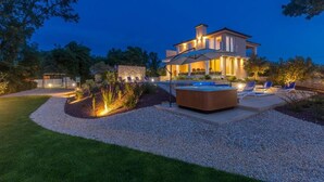 A modern house with a swimming pool, outdoor seating, and a well-lit garden at dusk.