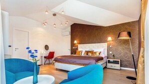 A modern bedroom with a large bed, two blue armchairs, a white side table, and a vase with flowers.