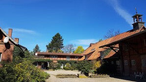 A courtyard with traditional brick buildings, a central garden, and a bell tower. - Large, bright vacation apartment in the Lüneburg Heath with pool house and 2 balconies (Oetzen)