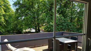 A balcony with a table and chairs, overlooking a garden with trees. - Large, bright vacation apartment in the Lüneburg Heath with pool house and 2 balconies (Oetzen)