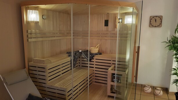 A sauna room with wooden benches, a glass partition, and a clock on the wall. - Large, bright vacation apartment in the Lüneburg Heath with pool house and 2 balconies (Oetzen)