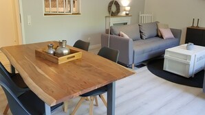 A modern living room with a wooden dining table, grey sofa, and a white side table. - Large, bright vacation apartment in the Lüneburg Heath with pool house and 2 balconies (Oetzen)