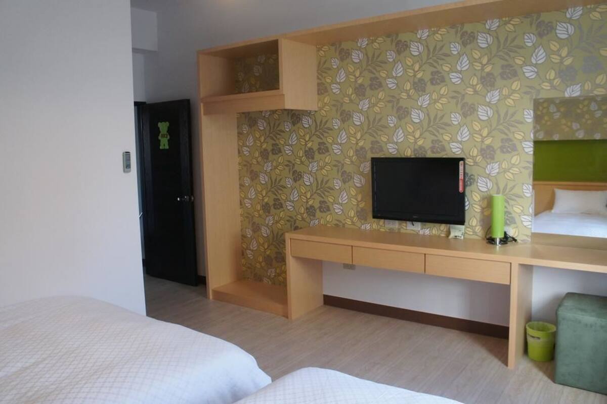 A hotel room with a bed, a desk with a television, and a patterned wall.
