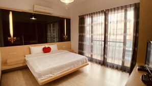A modern bedroom with a bed, a large mirror, a TV, and a window with sheer curtains. - Just Home (Magong)