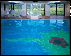 Een binnenzwembad met helder water, een jacuzzi en ligstoelen.