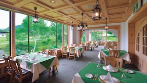 Ein Restaurant mit Holzbalkendecke, großen Fenstern mit Blick auf Grünflächen und gedeckten Tischen.
