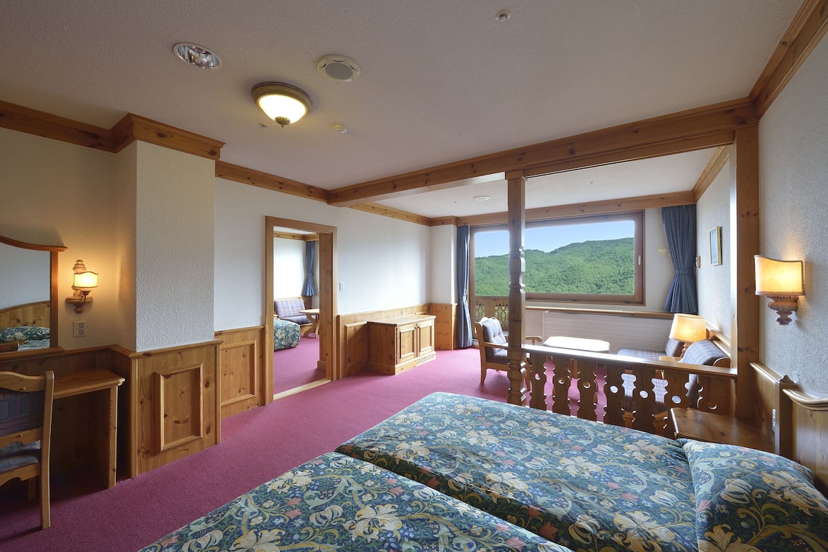 Une chambre dotée d’un grand lit, d’un bureau et offrant une vue sur un paysage verdoyant.