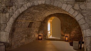 A stone-walled room with an arched doorway leading to a brighter area. Two lanterns are placed on the floor near the doorway.