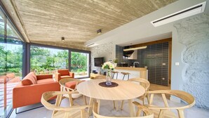 A modern living room with a wooden dining table, orange sofas, and a kitchen area with a stone backsplash.