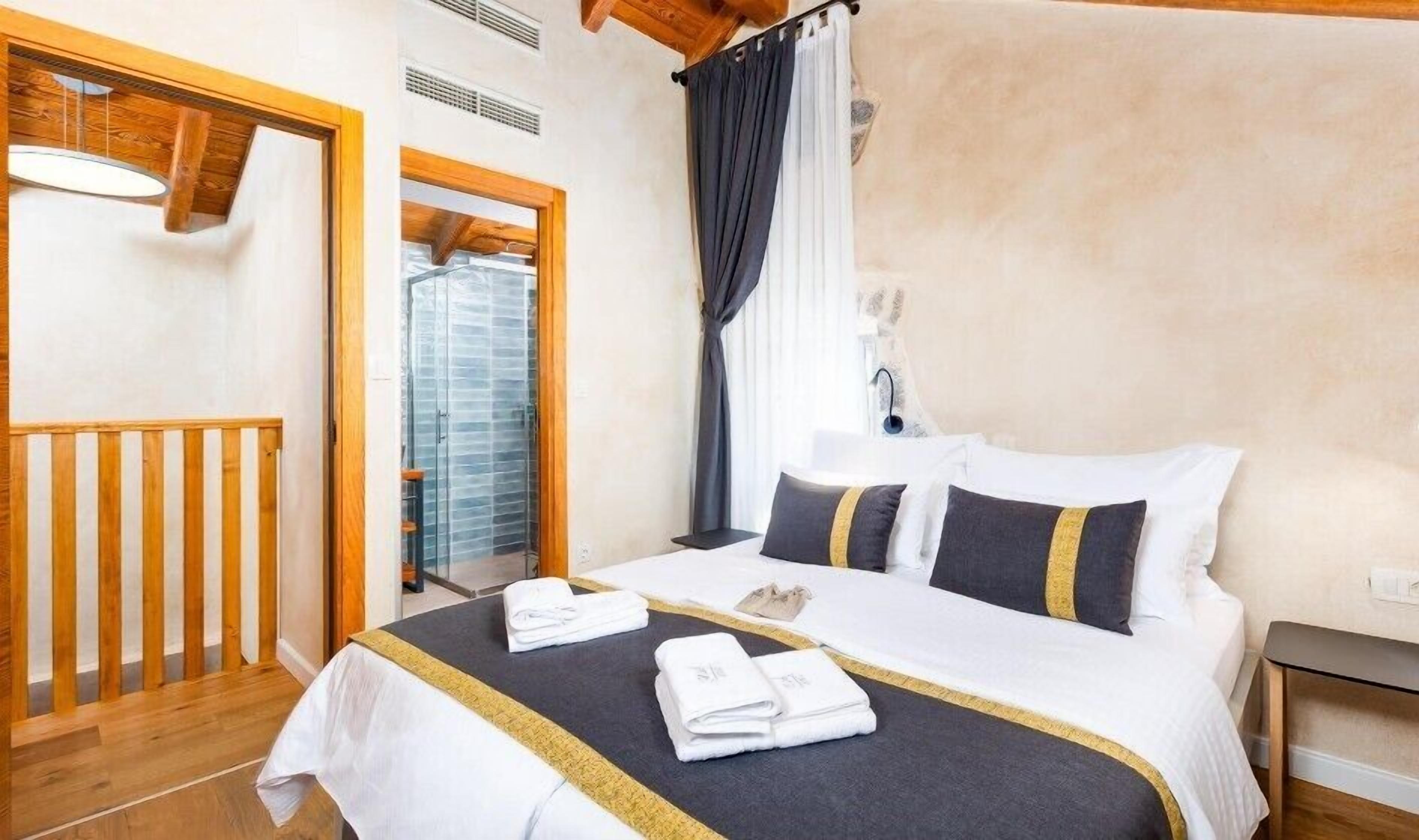 A hotel room with a bed, a wooden railing, a window with curtains, and a bathroom visible through the window.