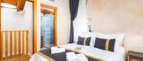 A hotel room with a bed, a wooden railing, a window with curtains, and a bathroom visible through the window.
