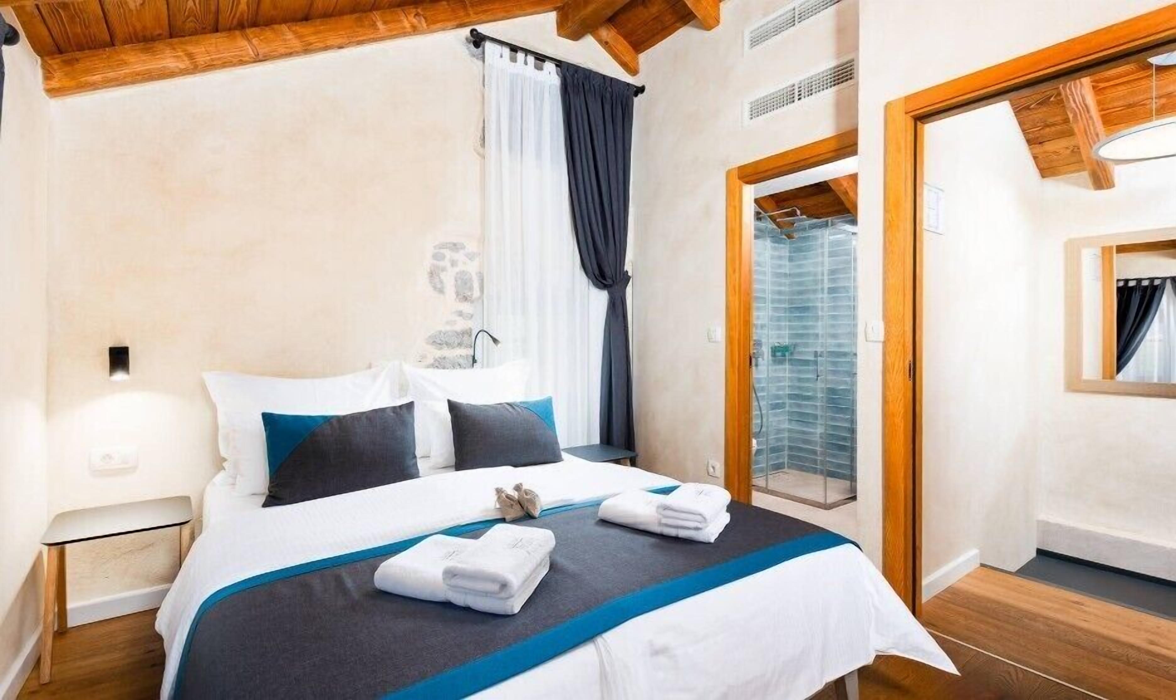 Una habitación de hotel con una cama, una mesita de noche, un ventanal con cortinas y una puerta que da a un balcón.