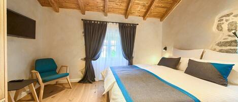 A bedroom with a wooden ceiling, a bed with a blue and white bedspread, a chair, and a window with curtains.