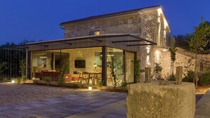 A modern house with a stone facade, a glass-enclosed patio, and a well-lit interior.