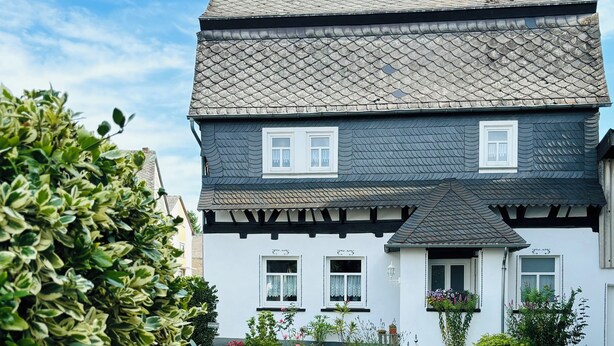 Une maison à deux étages, avec un toit recouvert de tuiles, des murs extérieurs blancs et une allée pavée en briques.