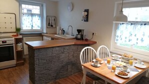 Une cuisine moderne avec un îlot central en pierre, des chaises blanches et des aliments pour le petit-déjeuner disposés sur la table.