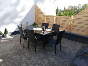 Une terrasse extérieure avec une table et des chaises, une bouteille de vin et un verre.