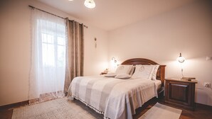 Une chambre à coucher avec un grand lit, deux tables de chevet, une commode, un tapis et une fenêtre avec des rideaux.