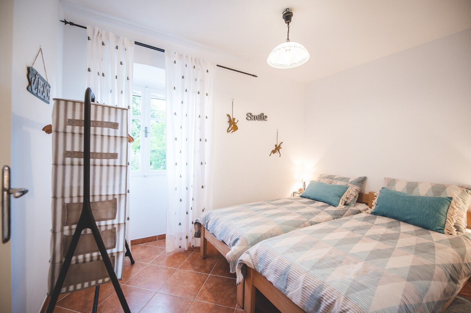 A bedroom with a bed, a ladder, a hanging light fixture, and a window with curtains.